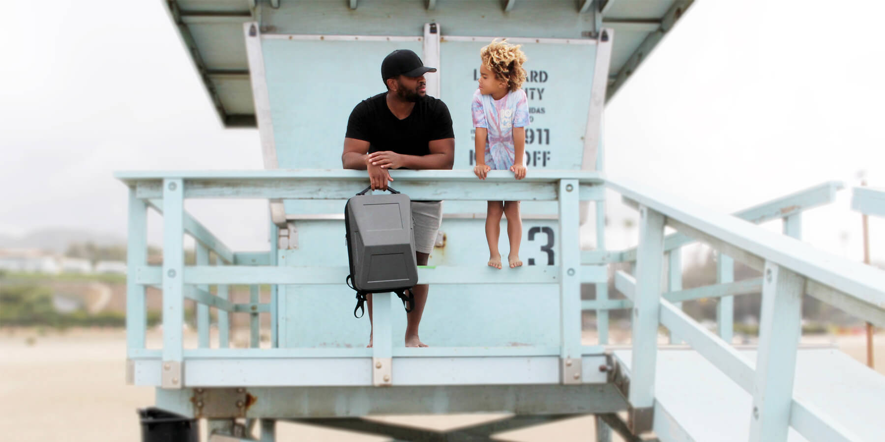 Riz and son on a lifeguard tower in malibu while holding a cyber backpack.